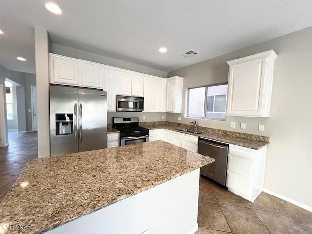 kitchen with sink, appliances with stainless steel finishes, white cabinetry, tile patterned flooring, and light stone counters