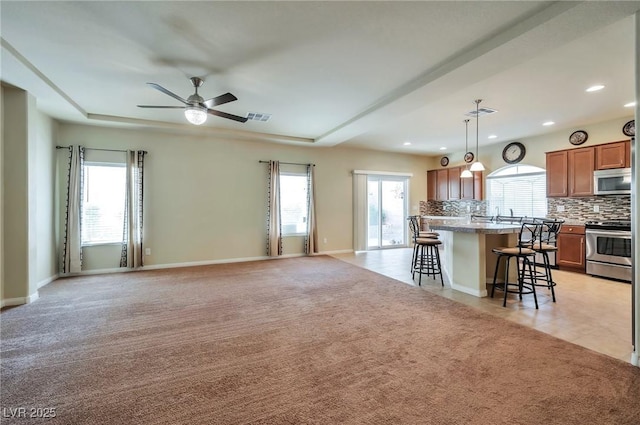 kitchen with a breakfast bar, decorative light fixtures, light colored carpet, stainless steel appliances, and a kitchen island with sink