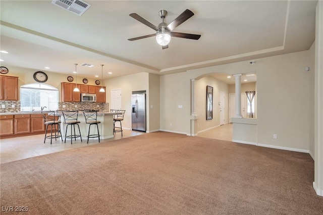 carpeted living room with decorative columns, a raised ceiling, and ceiling fan