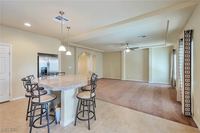 kitchen featuring stainless steel fridge, ceiling fan, hanging light fixtures, a kitchen breakfast bar, and light carpet