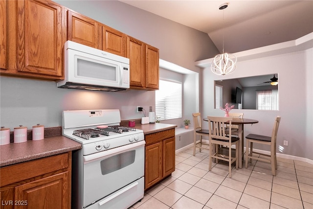 kitchen with lofted ceiling, light tile patterned floors, white appliances, a healthy amount of sunlight, and decorative light fixtures