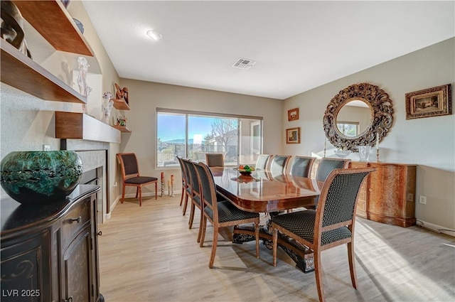 dining area featuring a tile fireplace and light wood-type flooring