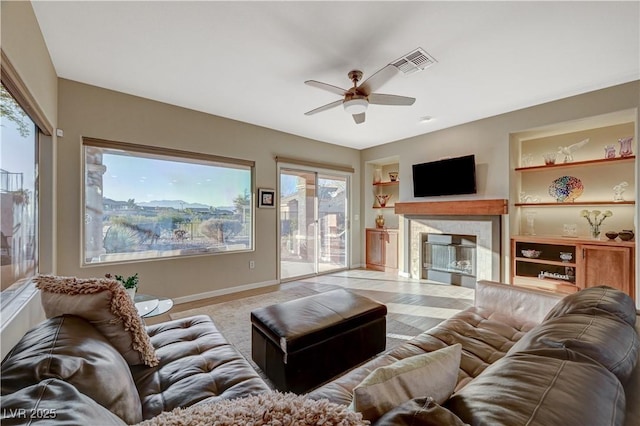 living room with a wealth of natural light, built in features, and ceiling fan