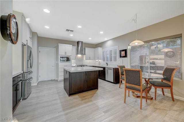 kitchen featuring pendant lighting, white cabinets, a center island, stainless steel appliances, and wall chimney exhaust hood