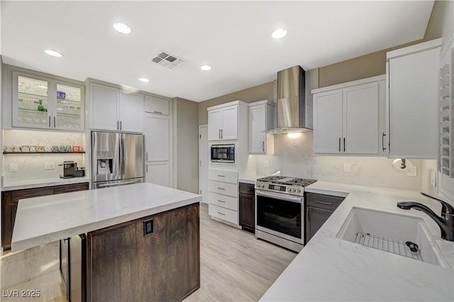 kitchen featuring sink, light stone counters, white cabinetry, stainless steel appliances, and wall chimney range hood