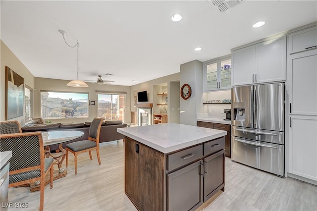 kitchen with stainless steel fridge, gray cabinetry, light stone countertops, decorative light fixtures, and light wood-type flooring