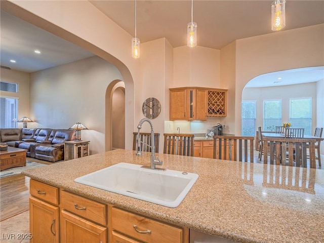 kitchen featuring light stone counters, sink, decorative light fixtures, and light hardwood / wood-style floors