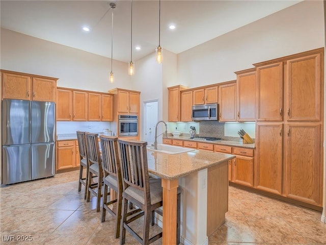 kitchen featuring a kitchen island with sink, sink, stainless steel appliances, and a kitchen bar