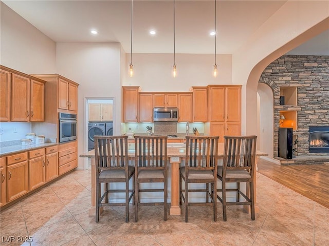 kitchen featuring pendant lighting, washer and clothes dryer, a breakfast bar area, stainless steel appliances, and light stone counters