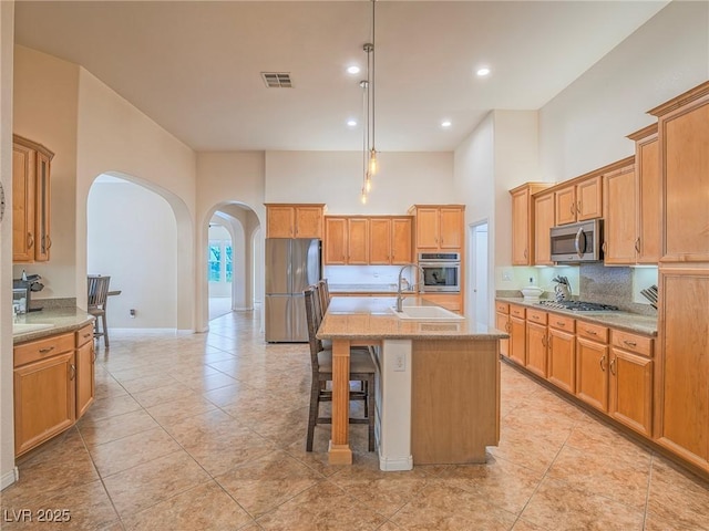 kitchen with appliances with stainless steel finishes, light stone countertops, sink, and a center island with sink