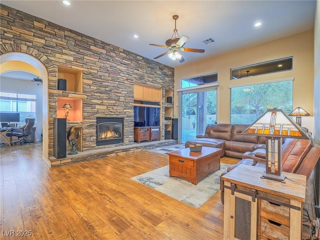 living room featuring ceiling fan, a stone fireplace, and light wood-type flooring