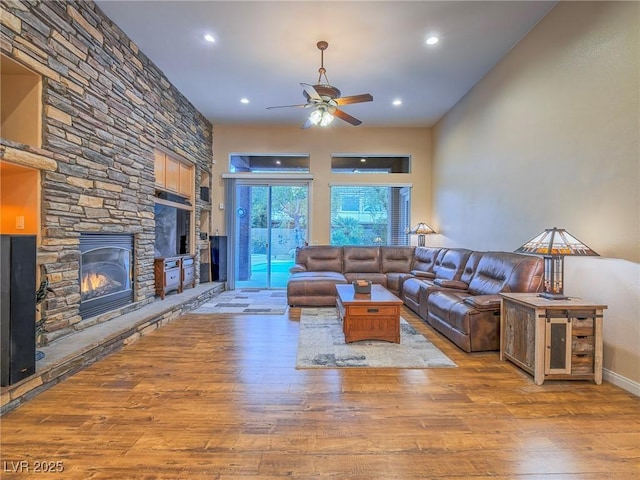 living room featuring hardwood / wood-style flooring, a stone fireplace, and ceiling fan