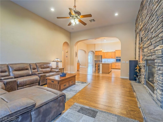 living room with ceiling fan, a stone fireplace, sink, and light wood-type flooring