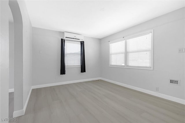 spare room with an AC wall unit and light wood-type flooring