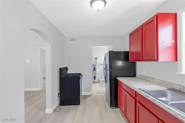 kitchen featuring sink, strapped water heater, light hardwood / wood-style floors, and black appliances