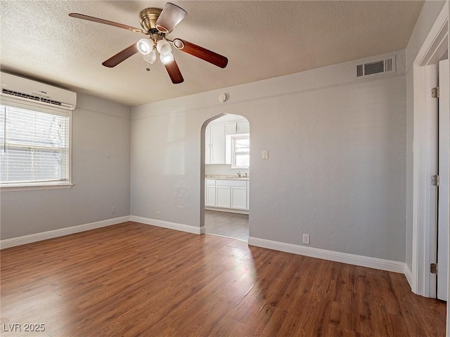 empty room featuring sink, ceiling fan, a wall mounted AC, a textured ceiling, and dark hardwood / wood-style flooring