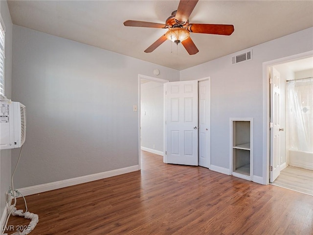 unfurnished bedroom with ensuite bathroom, multiple windows, wood-type flooring, ceiling fan, and a closet