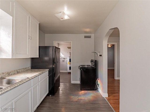 kitchen featuring sink, dark hardwood / wood-style floors, black refrigerator, and white cabinets