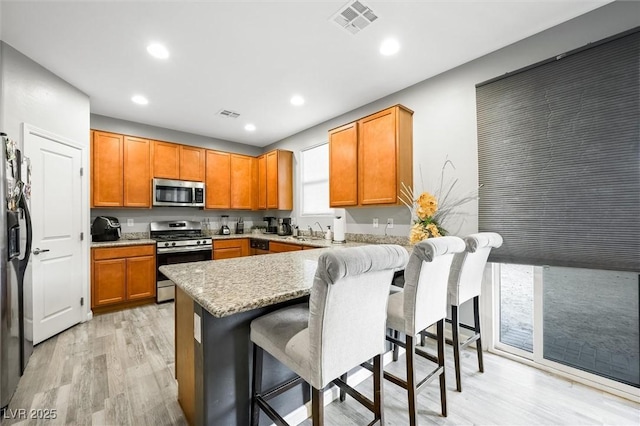 kitchen with a breakfast bar area, light stone counters, kitchen peninsula, stainless steel appliances, and light hardwood / wood-style floors