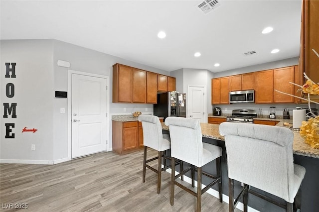 kitchen with light stone countertops, appliances with stainless steel finishes, a kitchen bar, and light hardwood / wood-style floors