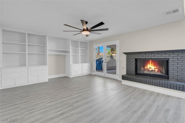 unfurnished living room featuring french doors, ceiling fan, a fireplace, and light hardwood / wood-style flooring