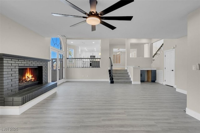 unfurnished living room featuring ceiling fan, a brick fireplace, and light hardwood / wood-style floors