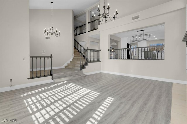 unfurnished living room featuring hardwood / wood-style flooring, a towering ceiling, and a chandelier