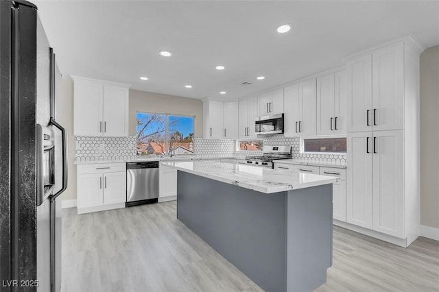 kitchen with white cabinetry, light stone counters, stainless steel appliances, and a kitchen island