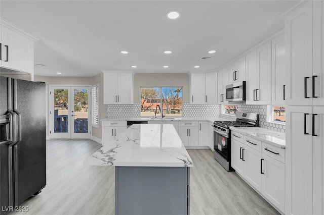 kitchen featuring a kitchen island, white cabinetry, decorative backsplash, black appliances, and light stone countertops