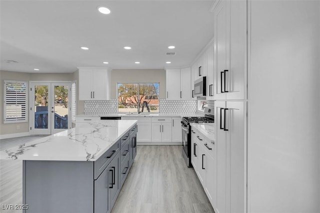 kitchen with white cabinetry, appliances with stainless steel finishes, light stone countertops, and a wealth of natural light