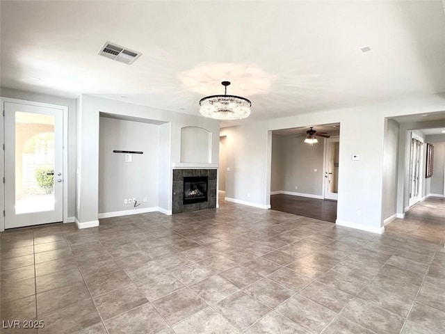 unfurnished living room with a tiled fireplace, tile patterned flooring, and ceiling fan with notable chandelier