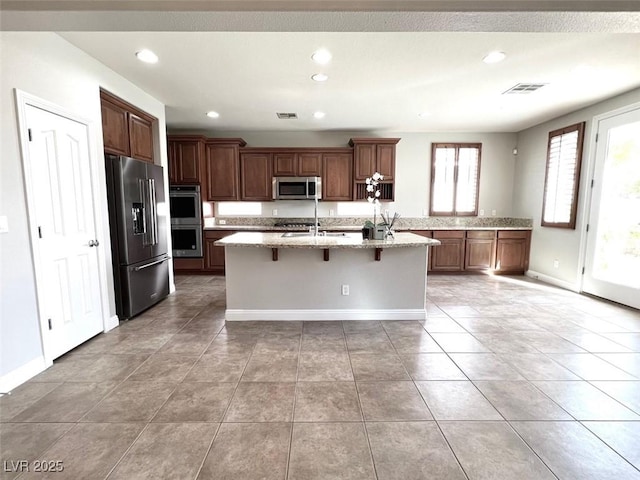 kitchen featuring an island with sink, sink, a kitchen breakfast bar, stainless steel appliances, and light stone countertops