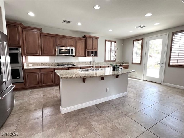 kitchen featuring sink, appliances with stainless steel finishes, a center island with sink, a kitchen bar, and light tile patterned flooring