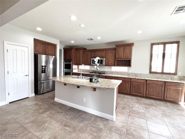 kitchen featuring a breakfast bar, sink, light stone counters, a center island with sink, and appliances with stainless steel finishes