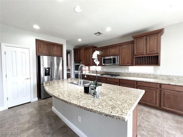 kitchen featuring sink, stainless steel appliances, an island with sink, and light stone countertops