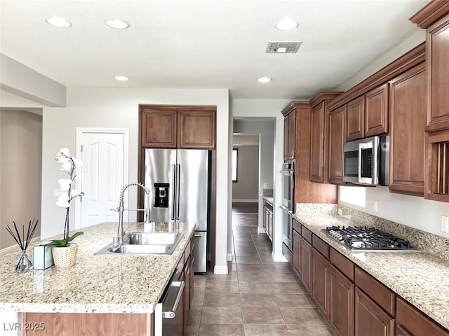 kitchen featuring appliances with stainless steel finishes, sink, light tile patterned floors, light stone counters, and a center island with sink