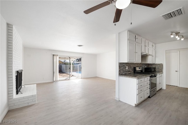 kitchen with stainless steel gas range oven, light hardwood / wood-style floors, white cabinets, a brick fireplace, and decorative backsplash