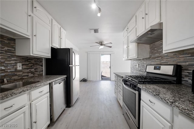 kitchen with dark stone countertops, appliances with stainless steel finishes, tasteful backsplash, and white cabinets