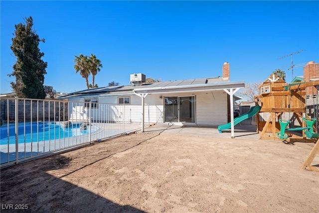 rear view of property with a fenced in pool, a playground, a patio, and solar panels