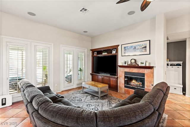 living room featuring a tiled fireplace, light tile patterned floors, and ceiling fan