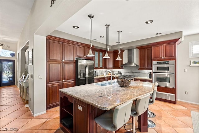 kitchen with sink, light tile patterned floors, appliances with stainless steel finishes, an island with sink, and wall chimney exhaust hood