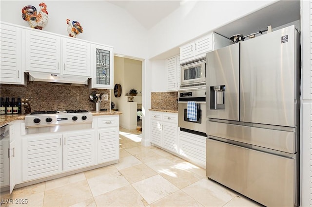 kitchen featuring white cabinetry, vaulted ceiling, stainless steel appliances, light stone countertops, and decorative backsplash