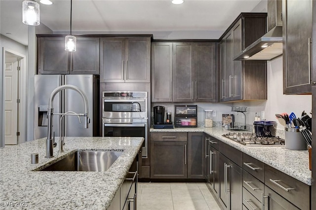 kitchen featuring wall chimney exhaust hood, sink, decorative light fixtures, stainless steel appliances, and light stone countertops