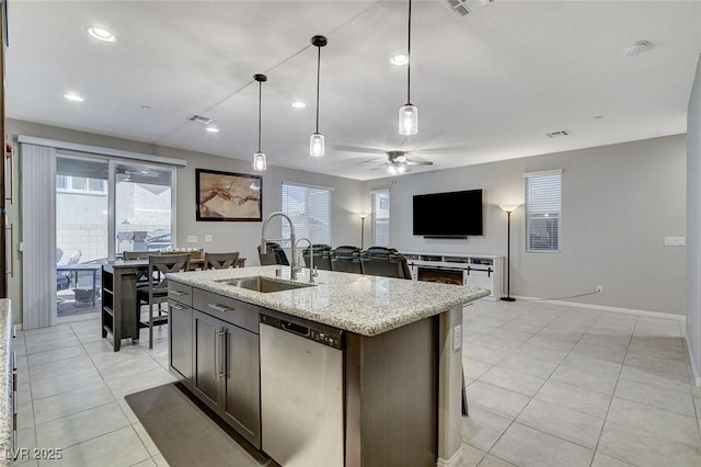 kitchen with pendant lighting, sink, stainless steel dishwasher, light stone counters, and a center island with sink