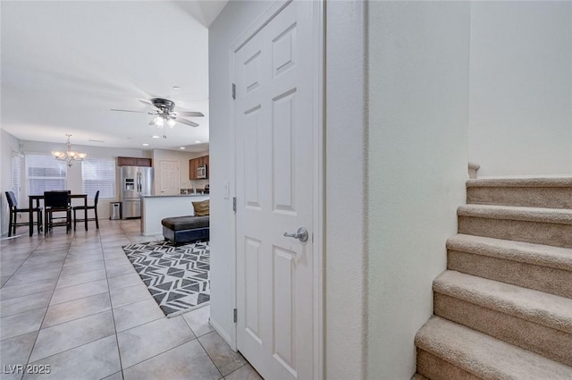 staircase with tile patterned floors and ceiling fan with notable chandelier