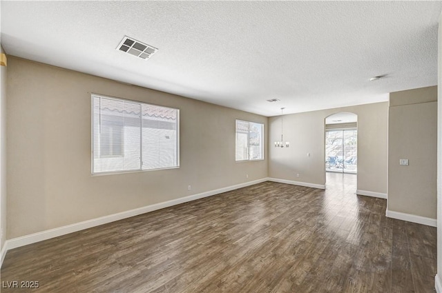 unfurnished room with a notable chandelier, dark wood-type flooring, and a textured ceiling