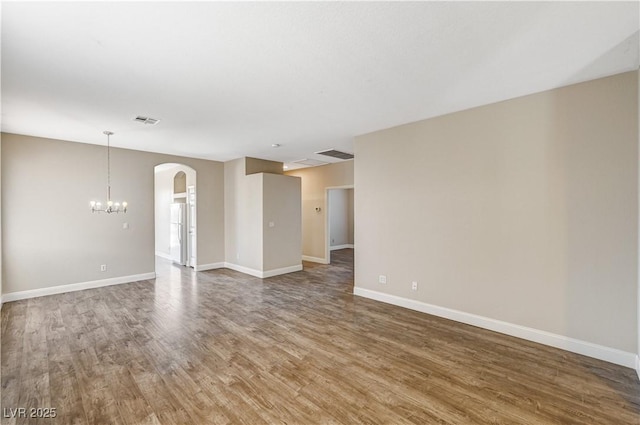 empty room with wood-type flooring and a notable chandelier