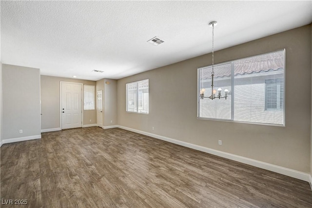 empty room with dark hardwood / wood-style flooring, a wealth of natural light, and a chandelier