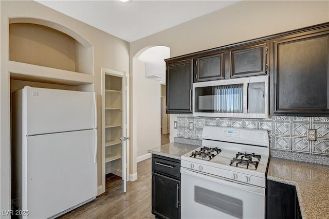 kitchen featuring tasteful backsplash, light stone countertops, dark brown cabinets, white appliances, and light hardwood / wood-style flooring