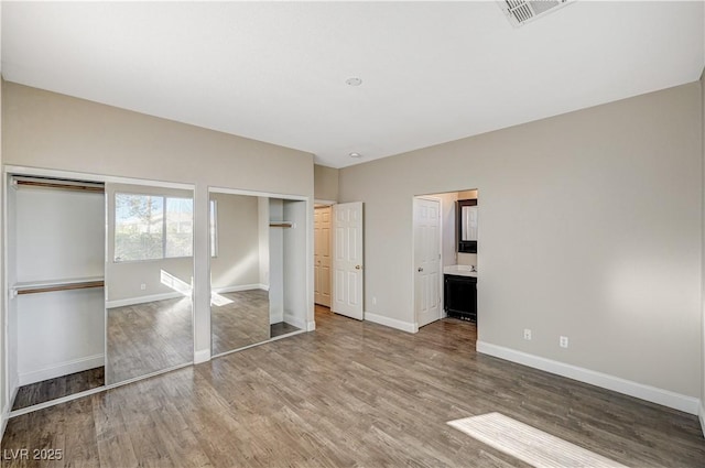 unfurnished bedroom with hardwood / wood-style floors, two closets, and ensuite bath